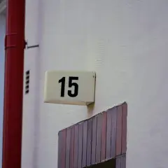 Tabliczka z numerem 15 na ścianie, obok czerwonej rury. Idealne wskazanie adresu dla najmu okazjonalnego.