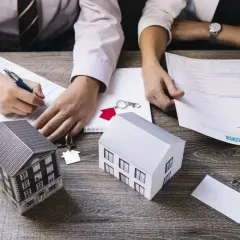 Dwie osoby analizują dokumenty, obok modele domów i klucze. To obrazuje, co to jest kredyt hipoteczny i jak go uzyskać.