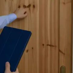 Ręka puka do drzwi, trzymając tablet. Może to być właściciel, który ma problem, bo lokator nie chce się wyprowadzić po zakończeniu umowy.