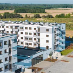 Nowa winnica Miękinia: nowoczesne bloki mieszkalne z balkonami, otoczone zielenią i parkingiem, na tle pól i lasu.
