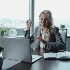 Kobieta przy biurku, z kulką papieru w dłoni, gestykuluje podczas wideokonferencji. Może to być frustracja związana z wypowiedzeniem umowy najmu mailem.