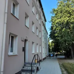 Budynek mieszkalny z oknami i drzwiami, obok drzewa i chodnik. To miejsce może być związane z art. 18 ustawy o ochronie praw lokatorów.