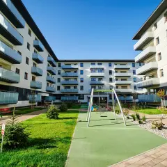 Nowoczesny **piano park** z placem zabaw i zielenią między budynkami mieszkalnymi.