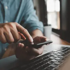 Mężczyzna sprawdza na telefonie, czy lokator może zawrzeć umowę na prąd, obok leży laptop.