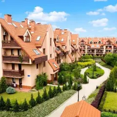 Osiedle Złota Podkowa: szeregowe domy z pomarańczowymi dachami, zadbane ogrody i kręte ścieżki tworzą sielski krajobraz.