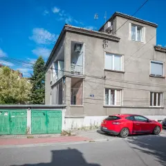 Szare apartamenty Bandtkiego z zielonymi garażami i czerwonym samochodem na tle błękitnego nieba.