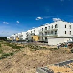 Nowe osiedle z białymi budynkami i balkonami, otoczone zielenią i placem budowy. To przyszłe eco berensona.