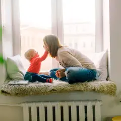 Mama i dziecko siedzą na parapecie. Wzór umowy najmu mieszkania dla rodziny z dzieckiem jest na książce.
