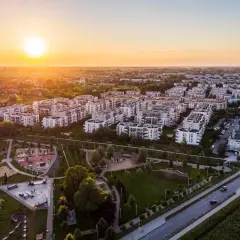 Zachód słońca nad nowoczesnymi osiedlami Białołęki. Widać bloki mieszkalne, park z placem zabaw i skateparkiem, drogi z samochodami.