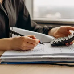 Kobieta z kalkulatorem i długopisem analizuje dokumenty, szukając wzoru podwyższenia czynszu najmu okazjonalnego.