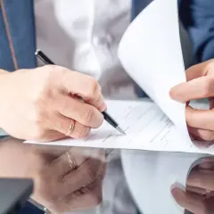 Mężczyzna w garniturze podpisuje dokumenty, co może oznaczać przedłużenie umowy najmu okazjonalnego.