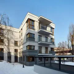 Nowoczesne osiedle oficerskie Kraków, z białymi fasadami i drewnianymi oknami, otoczone zimowym krajobrazem i nagimi drzewami.