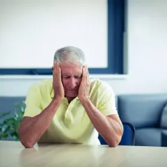 Zmartwiony starszy mężczyzna z rękami na skroniach. Może szukać wzoru pozwu o eksmisję dorosłego syna.