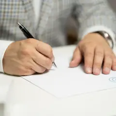 Mężczyzna w eleganckim garniturze podpisuje dokument. Czy w umowie najmu musi być PESEL?