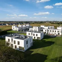 Nowoczesne osiedle eko falenty ronson z białymi domami i zielonymi trawnikami, w tle widać panoramę miasta.