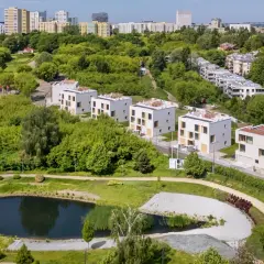 Nowoczesne domy w otoczeniu zieleni, z widokiem na miasto. Widać tu staw i ścieżki spacerowe, idealne do odpoczynku. To miejsce, gdzie życie w stylu sikorskiego vita jest możliwe.
