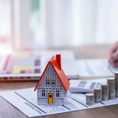 Model domu, stos monet i kalkulator na dokumencie "House Insurance". To symbol ubezpieczenia pomostowego, które chroni Twój dom.
