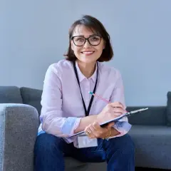 Uśmiechnięta kobieta w okularach, niezależny doradca finansowy, notuje coś na kartce.
