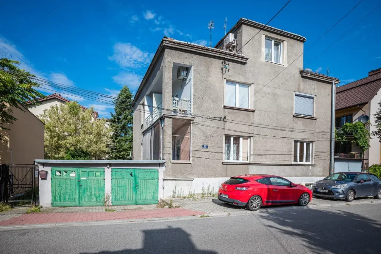 Szare apartamenty Bandtkiego z zielonymi garażami i czerwonym samochodem na tle błękitnego nieba.