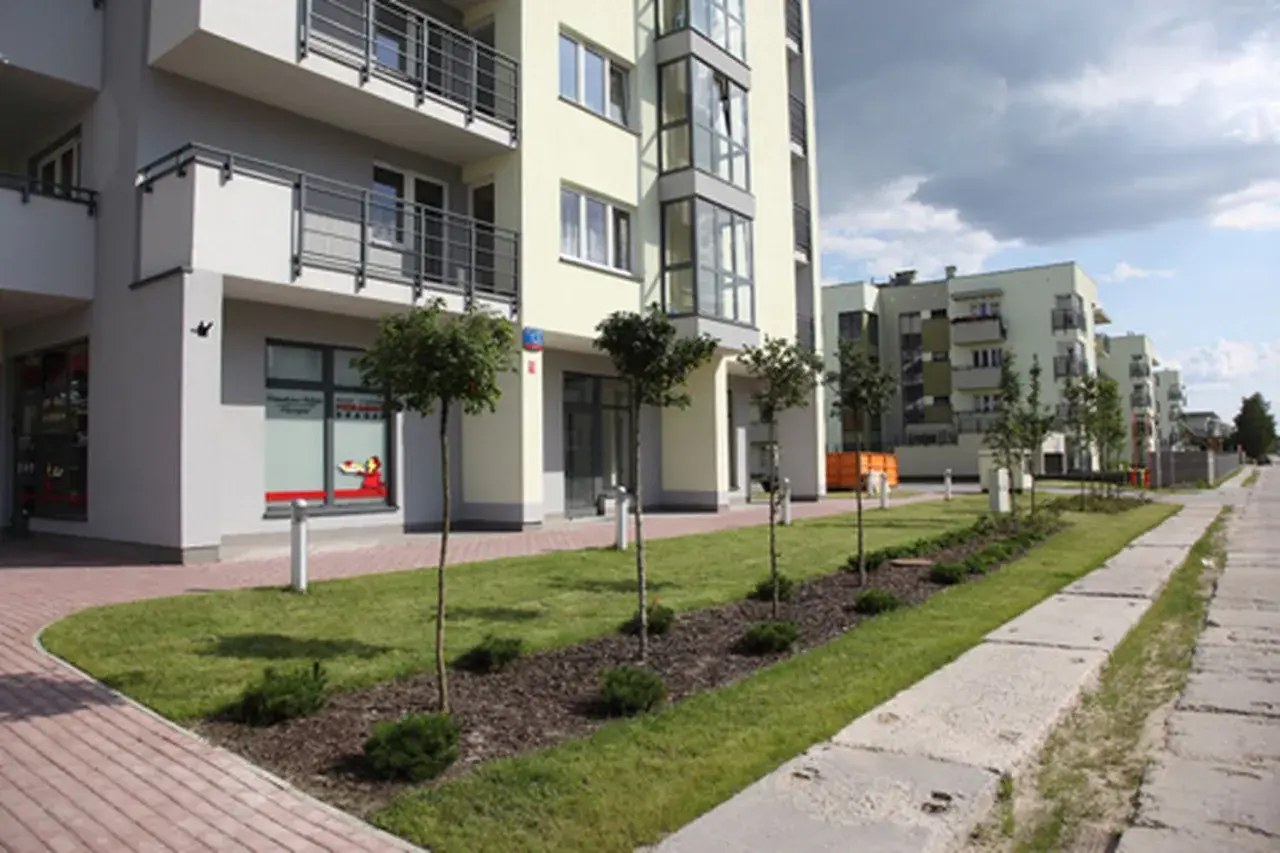 Nowoczesne budynki mieszkalne w stylu neowo bemowo z zielonymi skwerami i chodnikiem.