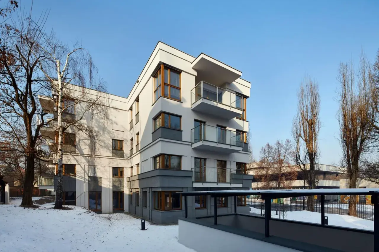 Nowoczesne osiedle oficerskie Kraków, z białymi fasadami i drewnianymi oknami, otoczone zimowym krajobrazem i nagimi drzewami.