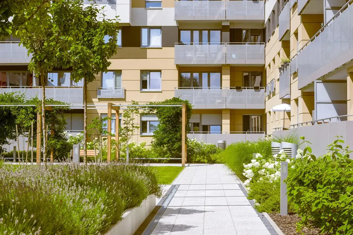 Ogród w stylu lagom z kwitnącą gardenią, zielenią i nowoczesnym budynkiem mieszkalnym.