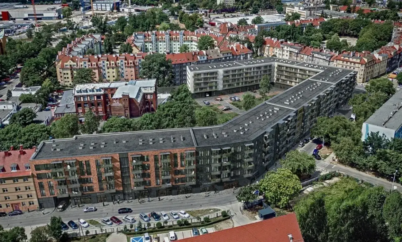 Nowoczesne osiedle mieszkalne w kształcie litery L, z ceglanymi i grafitowymi fasadami, otoczone zielenią. Nyska Wrocław.