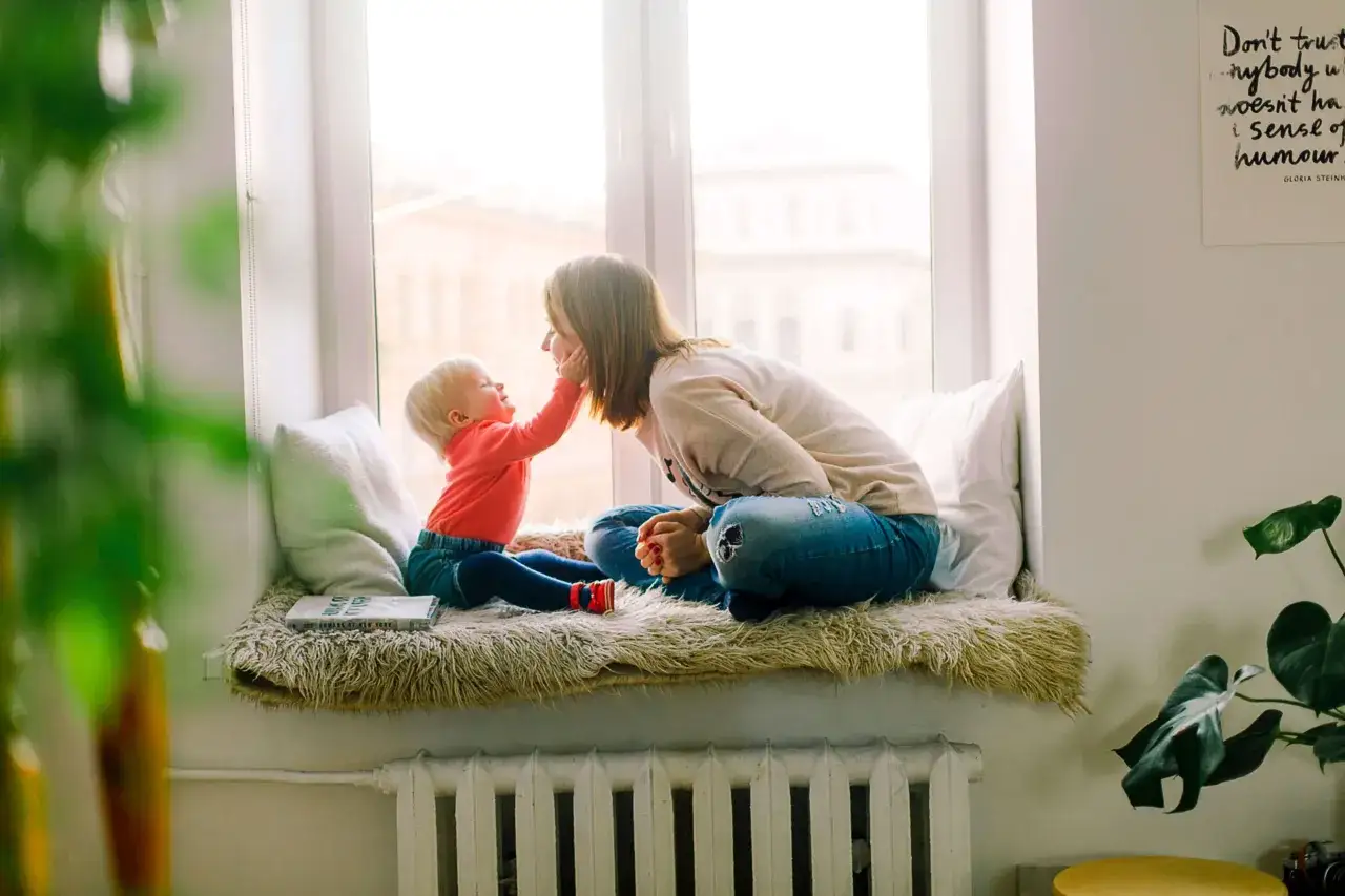 Matka z dzieckiem siedzą na parapecie. Dziecko dotyka policzka mamy. To idealny czas na spokojne chwile, jakby to był okres ochronny dla matki z dzieckiem wynajem.