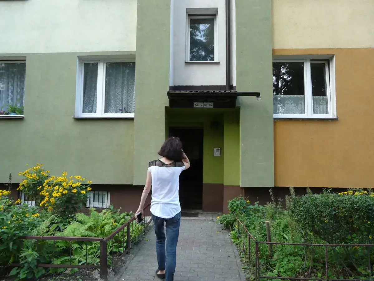 Smutny widok: eksmisja rodziny z dziećmi. Kobieta odchodzi od bloku, zostawiając za sobą dom.