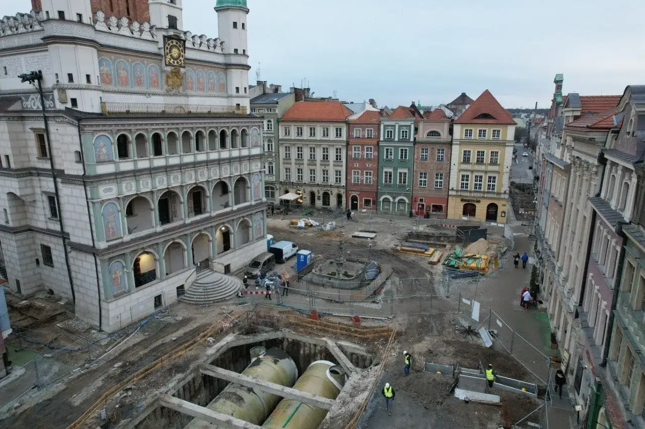 Stare miasto Poznań w trakcie prac budowlanych. Widać Ratusz, kolorowe kamienice i wykop z rurami.
